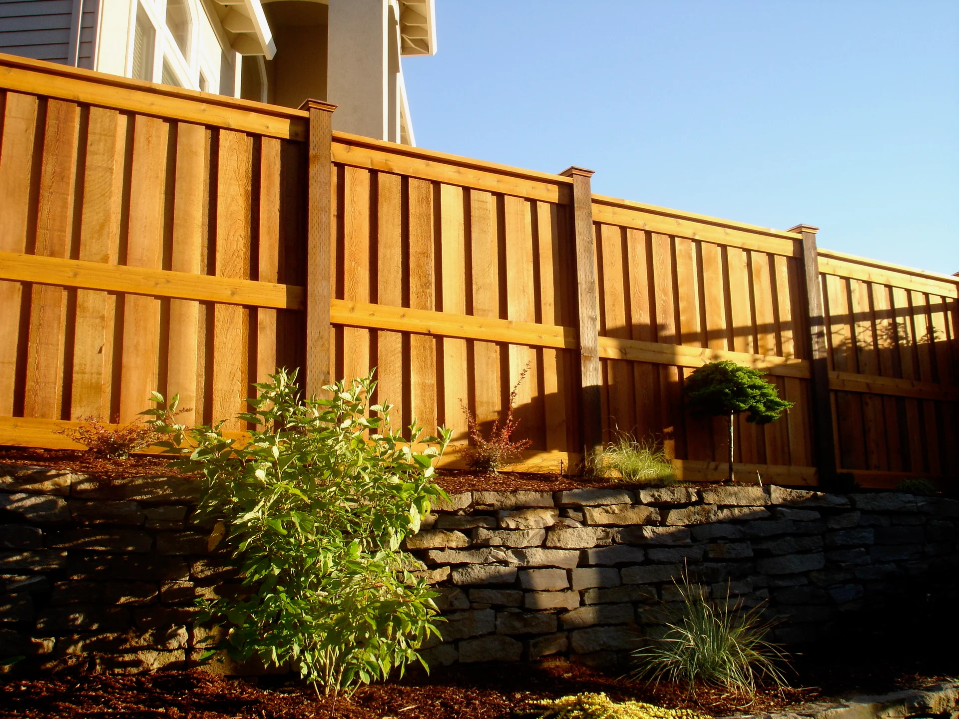 Finished neighbor-side view of a cedar privacy fence along a landscaped grade